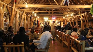 A restaurant with wooden beams and a thatched roof, featuring wooden benches and tables.