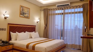 A hotel room with a large bed, a painting on the wall, and a view through the window.
