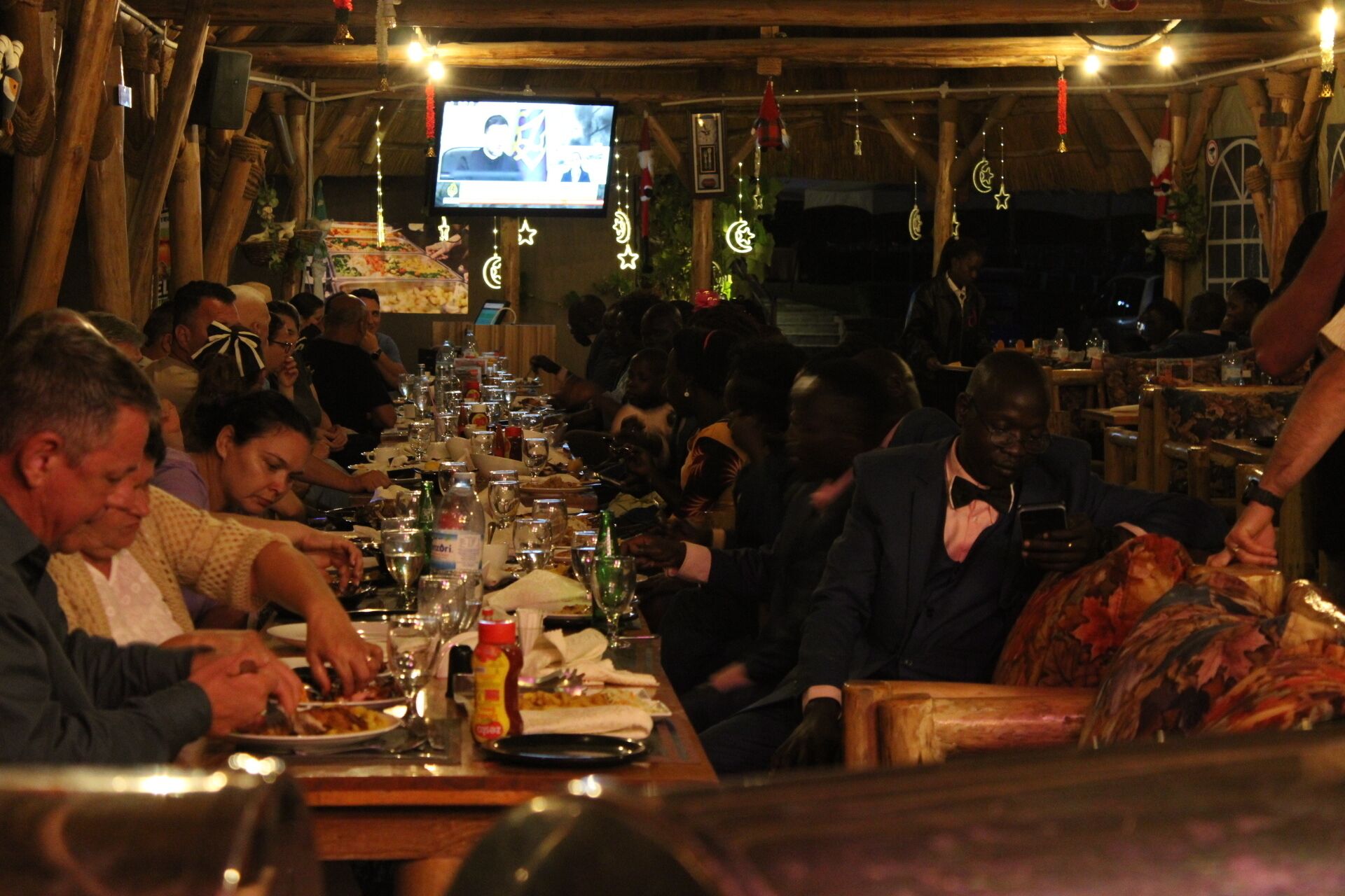 Un restaurante concurrido con mesas y sillas de madera, una pantalla de televisión y decoraciones festivas.