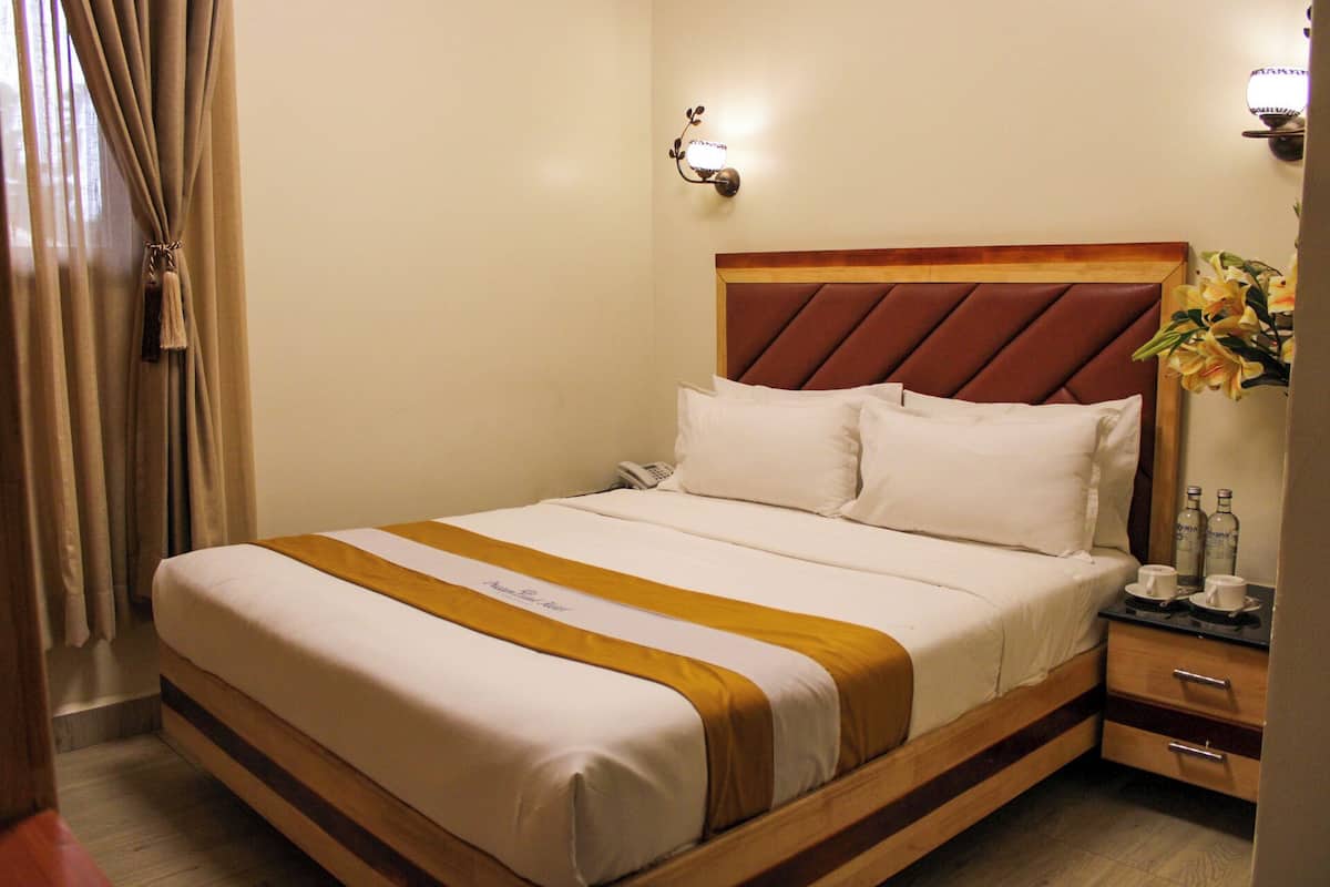 A hotel room with a bed, bedside table, lamp, and a vase with flowers.