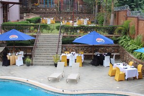 Uma área de refeições ao ar livre com mesas e cadeiras, piscina e escadaria que leva a um andar superior.