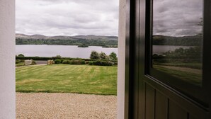 A view from a window overlooking a lake with a grassy area in the foreground and hills in the background.