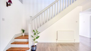 A staircase with wooden steps and a white handrail, leading to a landing with a radiator and a potted plant.
