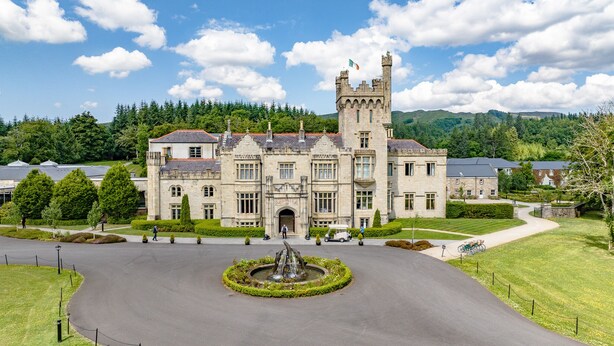 A large stone building with a central tower, surrounded by a well-maintained lawn and a circular fountain.