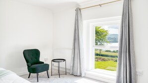 A room with a view of a green landscape through a window, a green armchair, a small round table, and a white radiator.