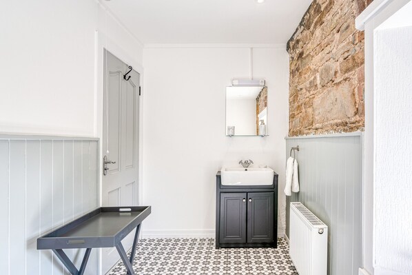 A bathroom with a white door, a small sink with a mirror above it, a towel hanging on the wall, and a radiator. - Luxury Farmhouse with Lough Eske Lake View | Nr Harveys Point/Lough Eske Castle (Barnesmore)