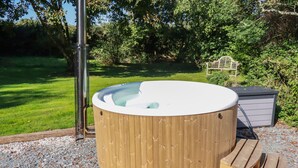 A wooden hot tub with a built-in heater, surrounded by gravel and a wooden deck. - Woodcutters (Launceston)