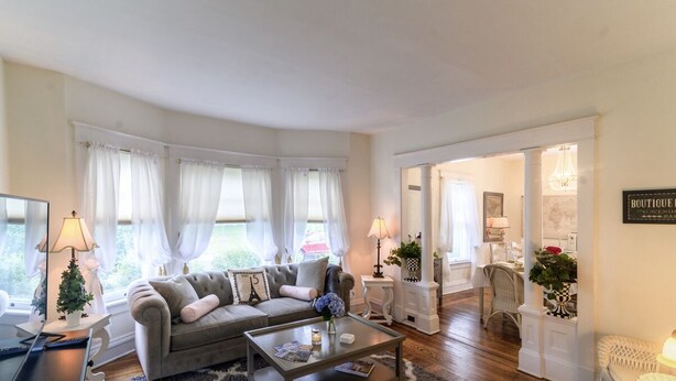 Sala de estar con sofá, mesa de centro y lámparas. Hay ventanas con cortinas y un candelabro.