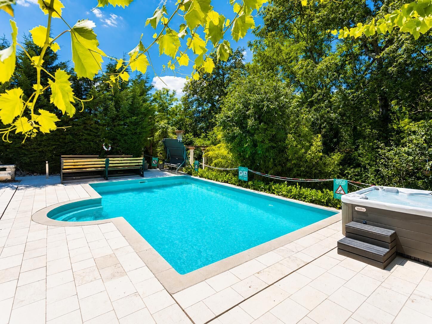En rektangulär swimmingpool med ett bubbelbad, omgiven av en kakelbeklädd terrass och en bänk.