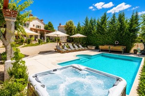 Una piscina con sillas de descanso y un jacuzzi, rodeada de vegetación y un edificio de piedra.