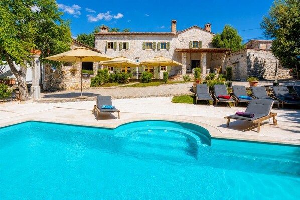 Una casa de piedra con piscina, mobiliario de exterior y sombrillas.