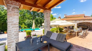 Eine Terrasse im Freien mit einem Steintisch, Stühlen und einem Pool im Hintergrund.