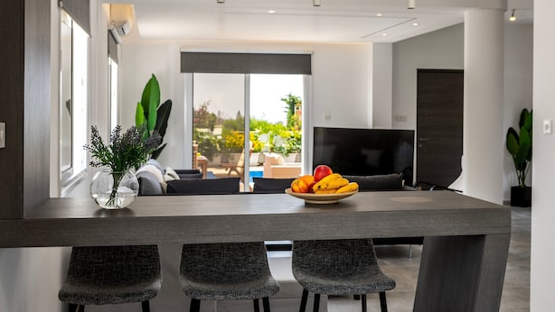 Una cocina moderna con una mesa de comedor, sillas, un cuenco de fruta y un florero con flores.