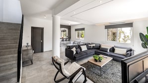 Una sala moderna con un sofá modular, un sillón mecedora, una mesa de centro y un televisor.