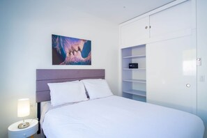 Ein Schlafzimmer mit Bett, Nachttisch, Lampe, einem Bild und einem Kleiderschrank.