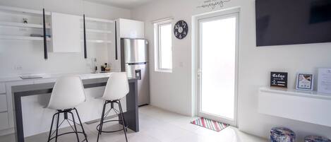 A modern kitchen with a central island, two bar stools, a refrigerator, and a wall-mounted clock.