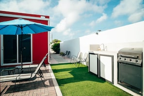 Eine Terrasse mit Grill, Stühlen und Sonnenschirm.