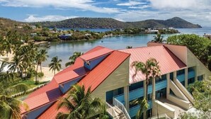 Un hotel de techo rojo, rodeado de exuberante vegetación y una masa de agua.