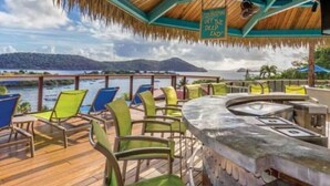 Terraza con sillas y zona de bar con vista a un cuerpo de agua y una montaña.