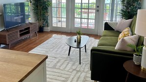 A living room with a wooden entertainment center, a green sofa, a coffee table, and a view through glass doors to an outdoor area. - Newly Renovated Water Front in Historic Cocoa Village with Pool! (Cocoa)