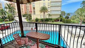 A wooden deck with a pool table and chairs, overlooking a swimming pool and a view of a multi-story building with balconies. - Newly Renovated Water Front in Historic Cocoa Village with Pool! (Cocoa)