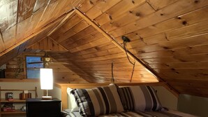 A cozy attic bedroom with a sloped ceiling, a bed with striped bedding, a bedside table with a lamp, and a window with a view.