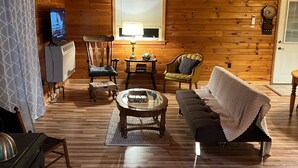 A cozy cabin interior with wooden walls, a fireplace, a television, and a comfortable seating area.