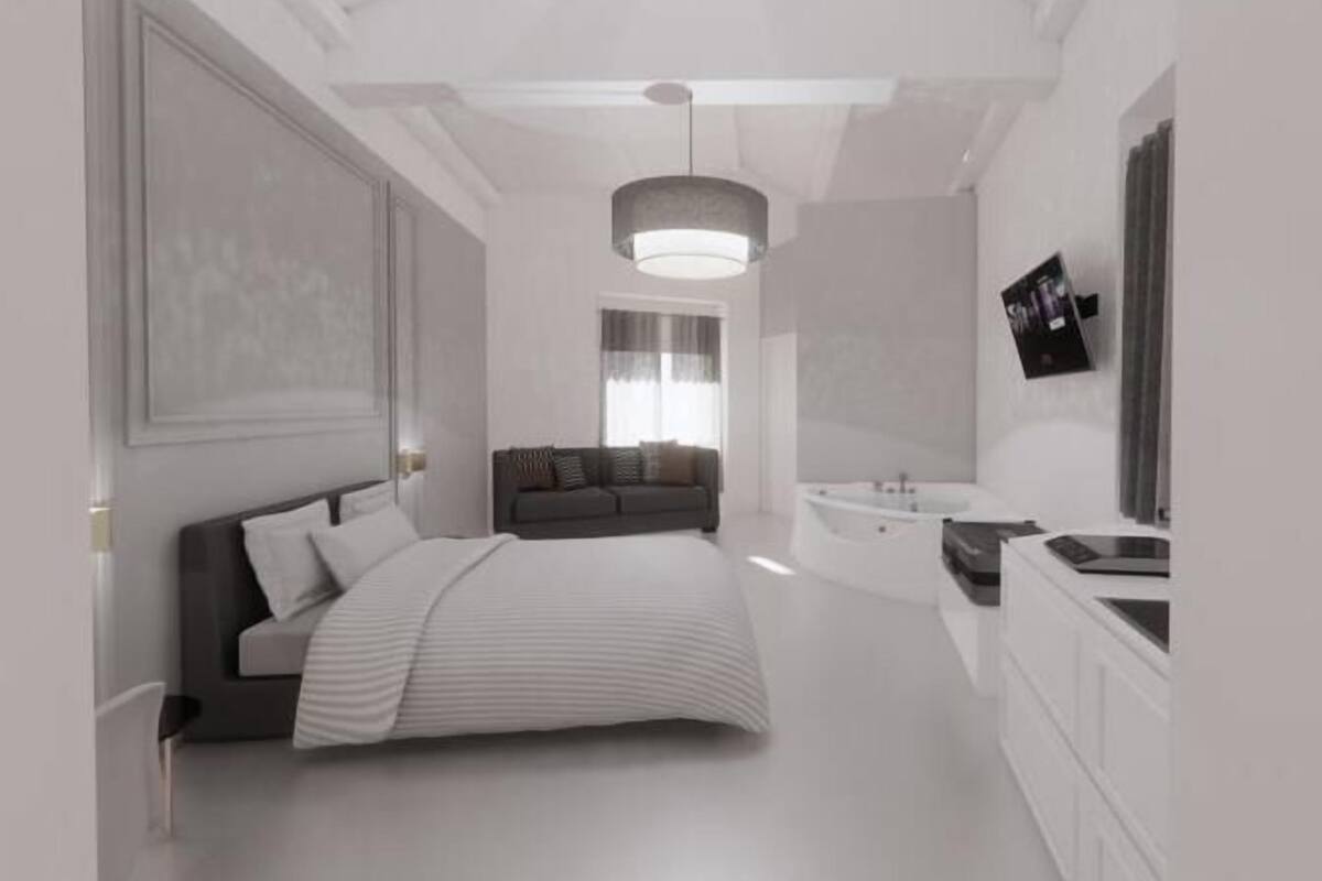 A modern bedroom with a large bed, a sofa, a bathtub, and a vanity.