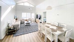 Un ampio soggiorno con soffitto alto, una zona pranzo con mobili bianchi e un'ampia finestra che offre luce naturale.