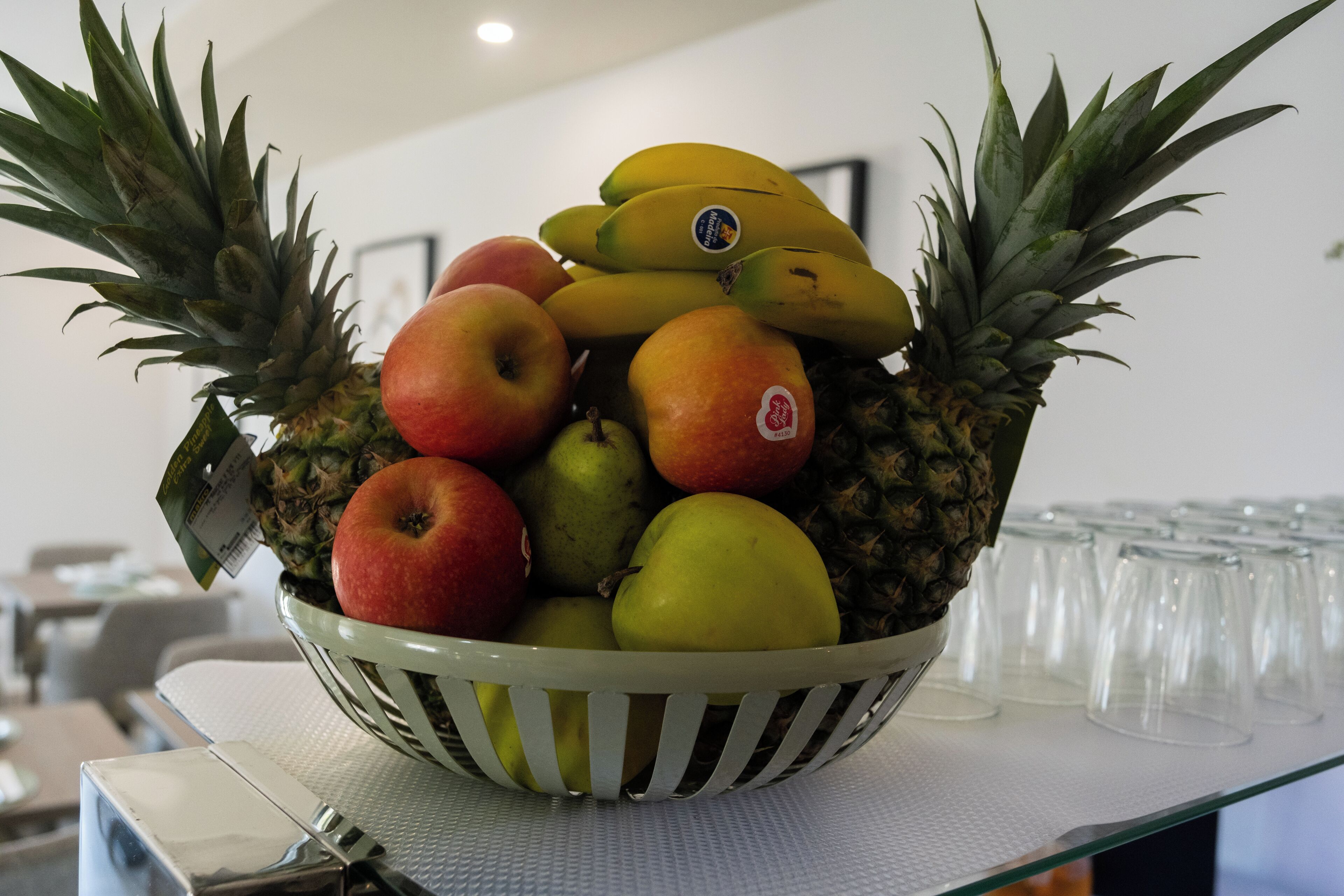 Un frutero con manzanas, plátanos y una piña sobre una mesa.