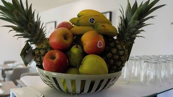 Un frutero con manzanas, plátanos y una piña sobre una mesa.
