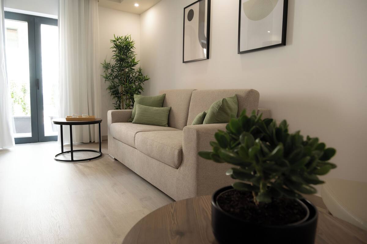 A modern living room with a beige sofa, green cushions, a round coffee table, and a potted plant.