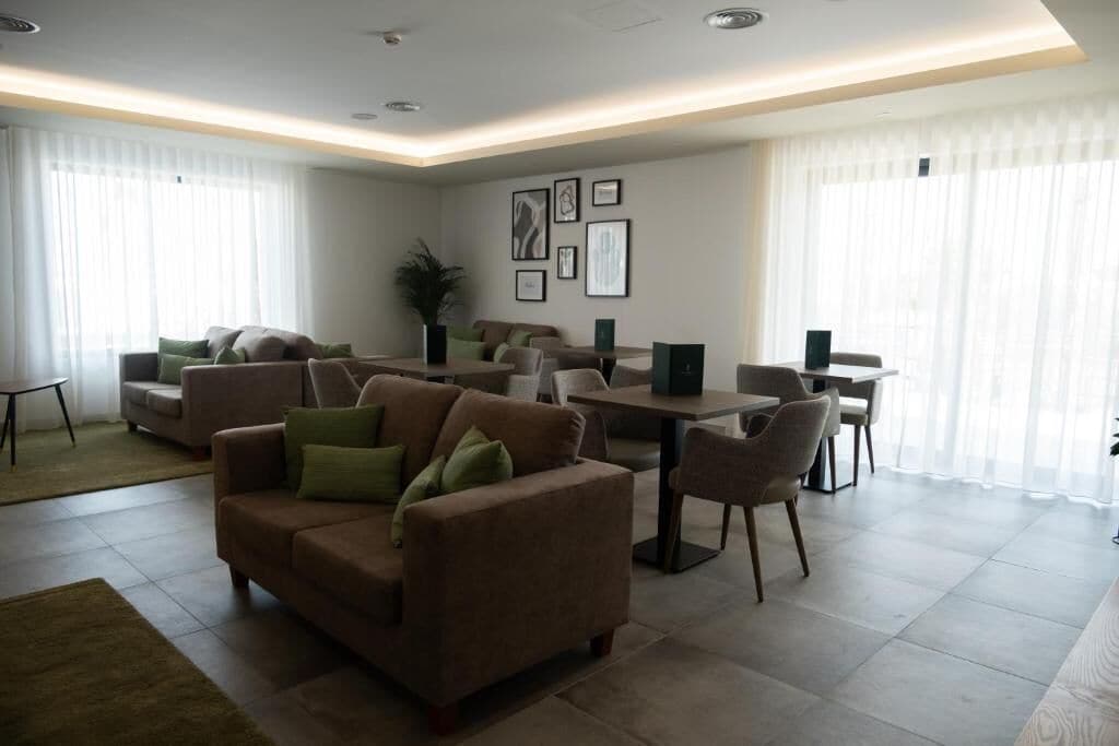Uma sala de estar moderna com um sofá marrom, uma mesa de jantar e cadeiras. Há quadros nas paredes e uma planta no canto.