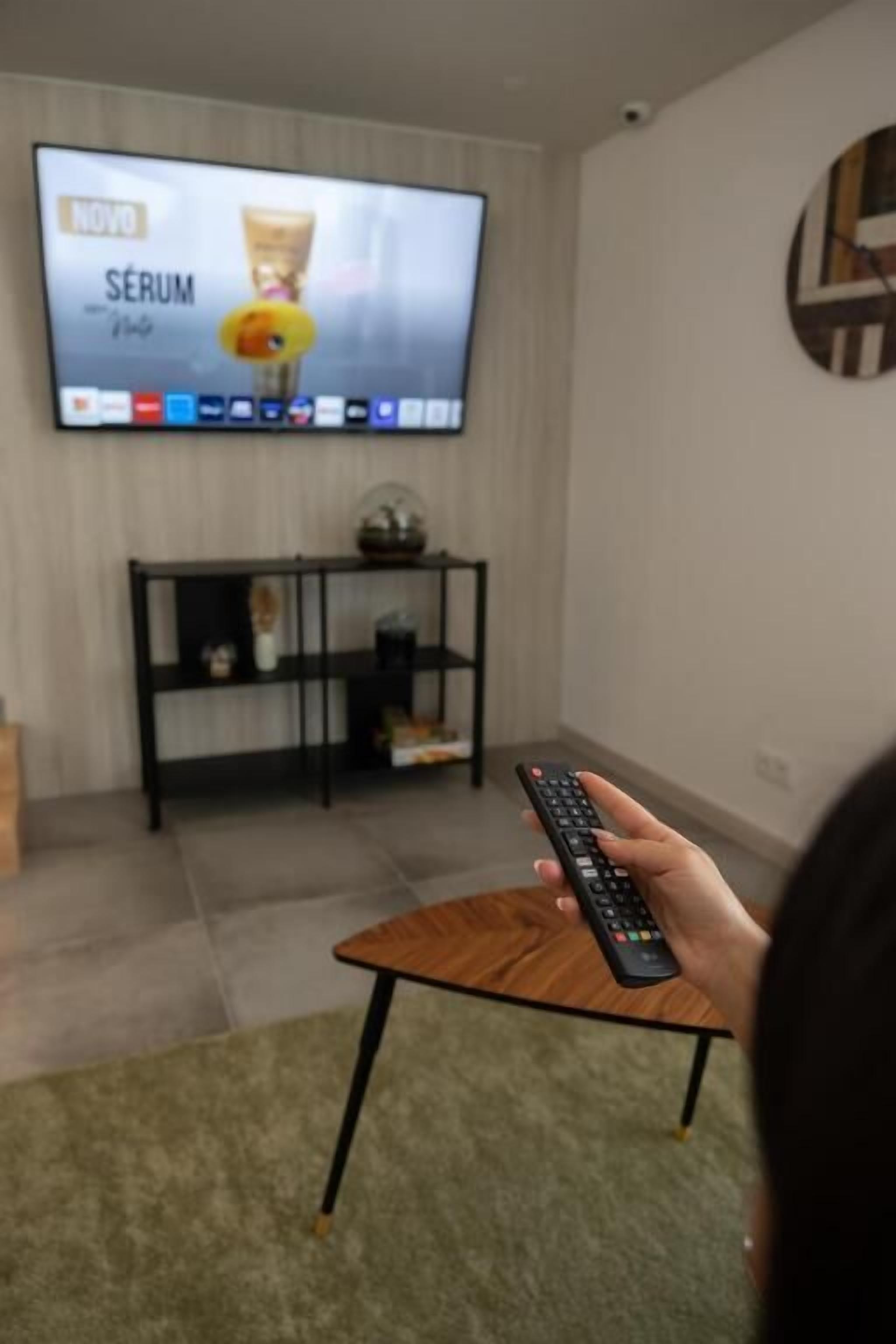 A living room with a television mounted on the wall displaying an advertisement. A person is holding a remote control.
