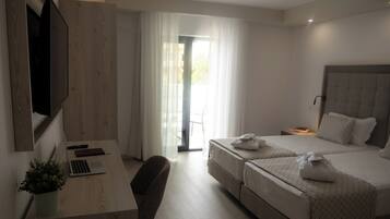 Habitación de hotel moderna con un escritorio de madera, una computadora portátil, una silla, dos camas con toallas y un televisor montado en la pared.