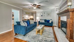 Ein Wohnzimmer mit zwei blauen Sofas, einem Holztisch, einem Kamin und einem Deckenventilator.