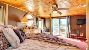 Een slaapkamer met een groot bed, een plafondventilator, een kroonluchter en uitzicht op het omliggende landschap.