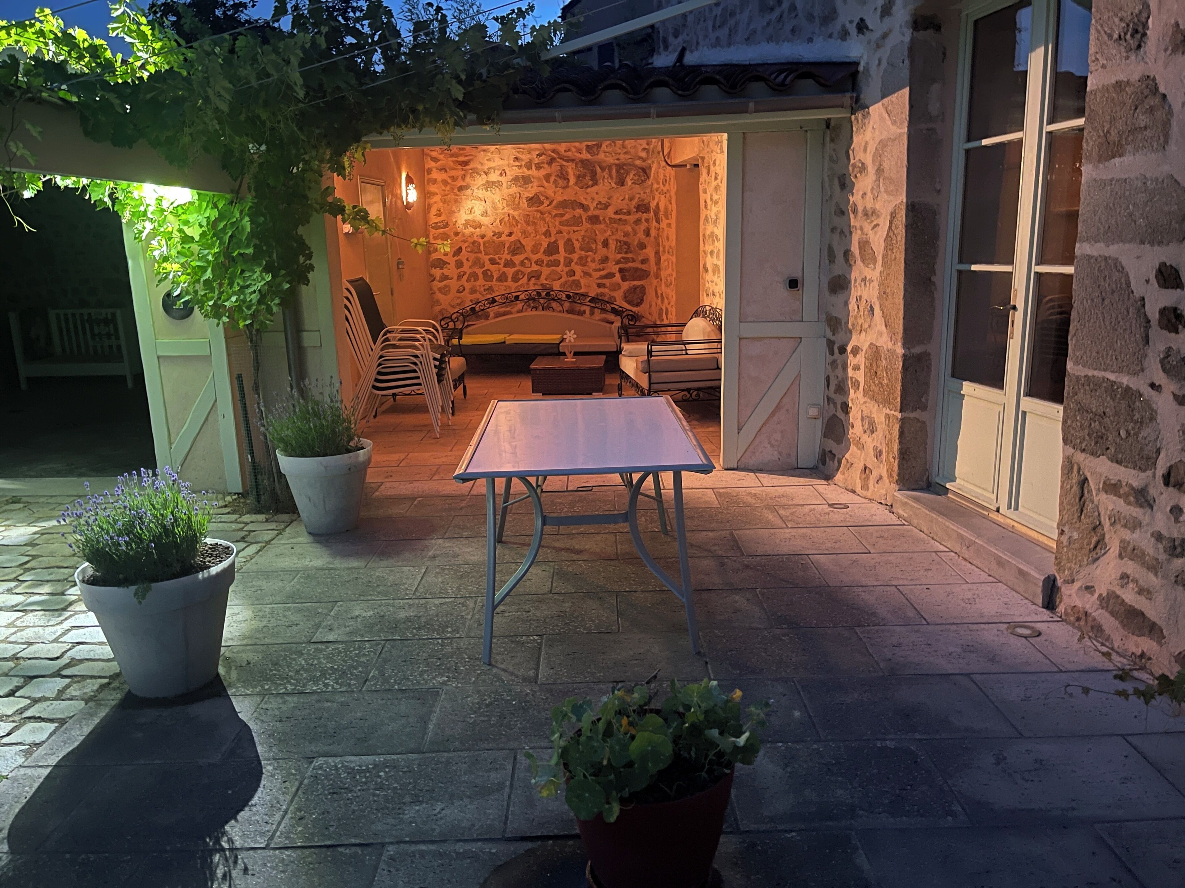 Un espace extérieur aménagé en patio, avec un mur en pierre, une table, des chaises et des plantes en pot.