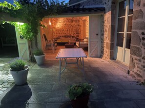 Un patio al aire libre con pared de piedra, una mesa, sillas y plantas en macetas.