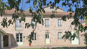 Un edificio in pietra con tetto in tegole, un prato verde e un tavolo in metallo con sedie in primo piano.