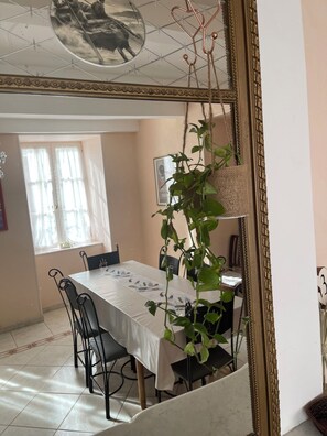A dining area with a table set for four, chairs, a hanging plant, and a framed picture on the wall.