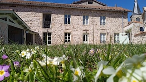 Un edificio in pietra con diverse finestre e un balcone, circondato da un'area verde con fiori.