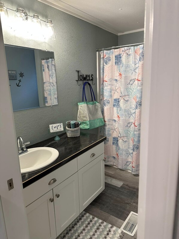 A bathroom with a white sink, a mirror, a towel rack, and a shower curtain with a nautical pattern. - Weekend Get Away (Sibley)