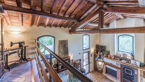 A rustic interior with exposed wooden beams, a sewing machine, a fireplace, and a kitchen area with wine bottles. - Fienile di Fabio by Geco Vacation Rentals (Vaiano)