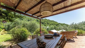 An outdoor patio with a wooden table and wicker chairs, surrounded by lush greenery and a clear view of the hills. - Fienile di Fabio by Geco Vacation Rentals (Vaiano)