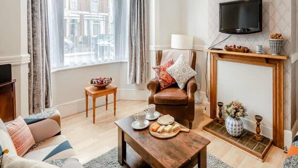 A cozy living room with a leather armchair, a wooden coffee table, a fireplace, and a television mounted on the wall.