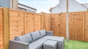 A sectional outdoor sofa with cushions, a wooden fence, and a grassy lawn.