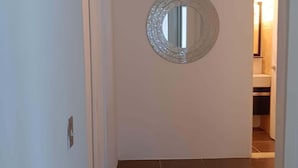 En gang med et rundt spejl på væggen, der fører til et badeværelse med toilet og håndvask.