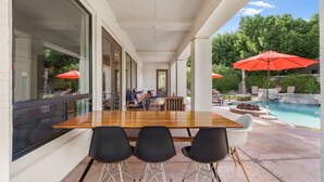 An outdoor patio with a wooden table and black chairs, overlooking a swimming pool and greenery. - Pool*Spa*Games*Golf*Polo*Festivals*4BR+2BR Casita (Indio)
