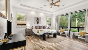 A modern bedroom with a bed, bedside tables, a desk, and a large window with a view of greenery. - Pool*Spa*Games*Golf*Polo*Festivals*4BR+2BR Casita (Indio)